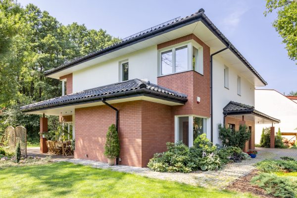 Red brick house with terrace and green grass and trees during summer