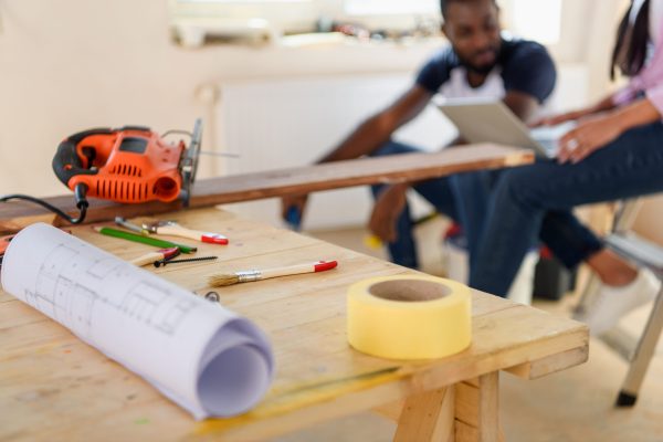 selective focus of wooden table with blueprint and couple sitting behind during renovation at home