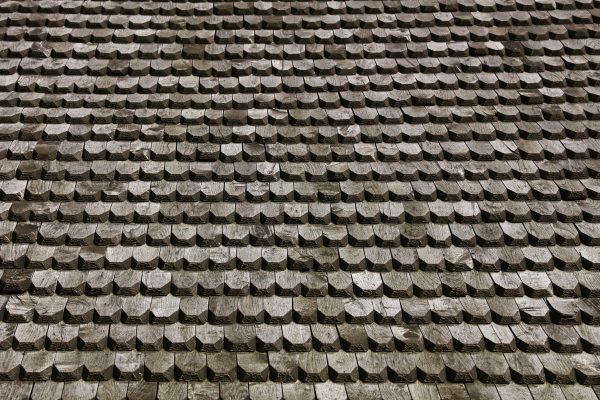 Wooden roof shingles are forming a repeating pattern, adding a touch of rustic charm and creating a visually appealing old texture on a sloped architectural structure