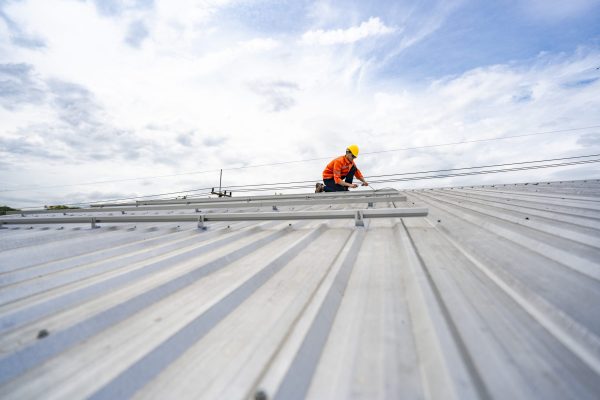Technician in safety uniform and helmet kneeling on a rooftop, using a drill for precise installation work. A scene highlighting safety, professionalism, and technical expertise in construction.